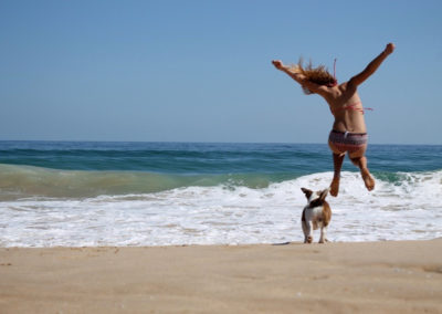 Girl Jumps On Beach With Dog
